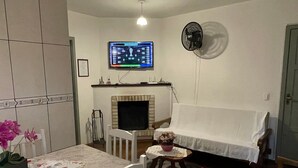 A living room with a television mounted on the wall, a fireplace, a dining table with chairs, and a small side table with a plant.