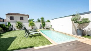 A swimming pool with a wooden deck, a grassy area, and a white building with a tiled roof. - Beautiful Montpellier Villa With Pool (Montpellier)