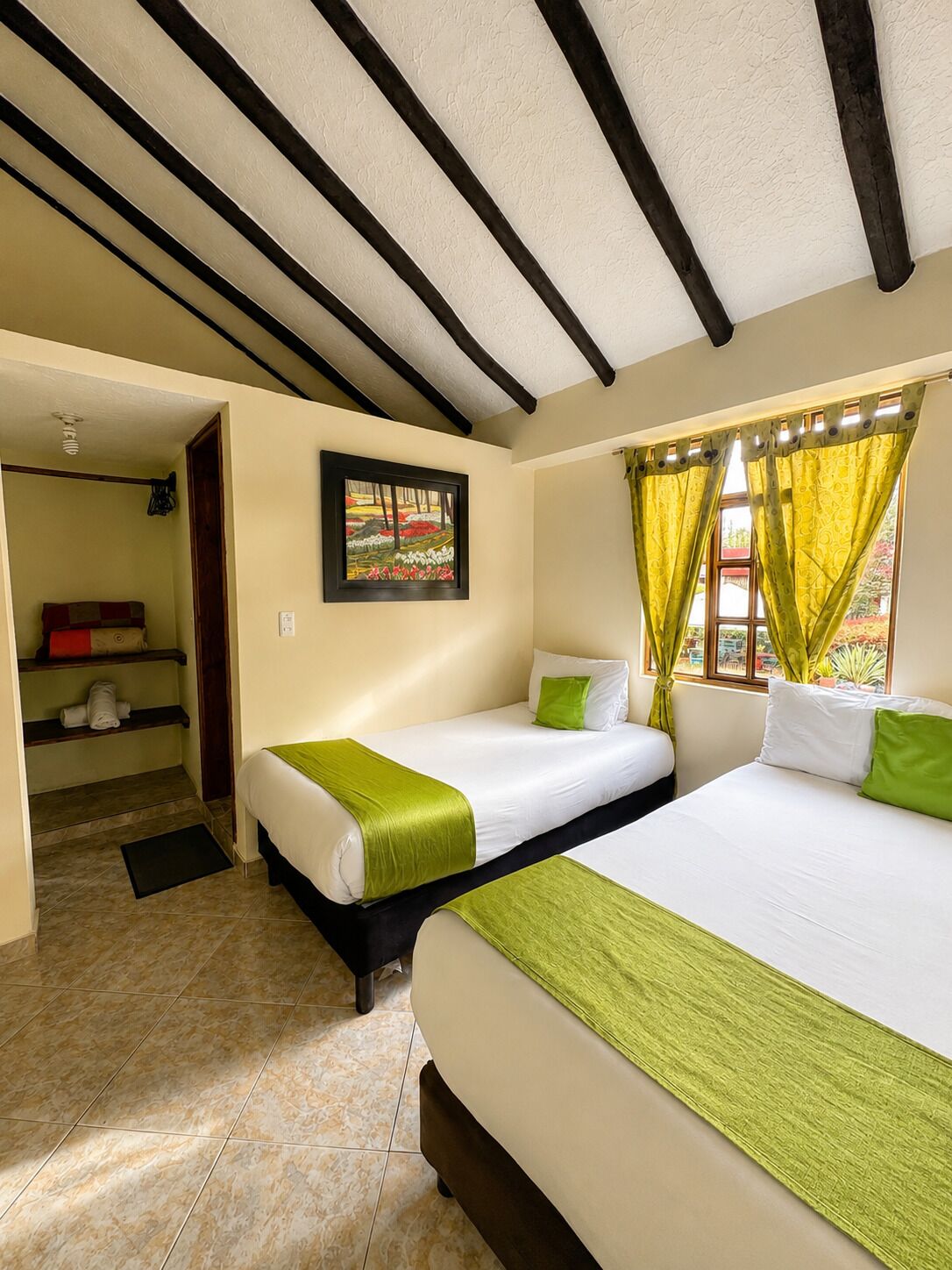 Quarto de hotel com duas camas, um quadro na parede e uma janela com cortinas.