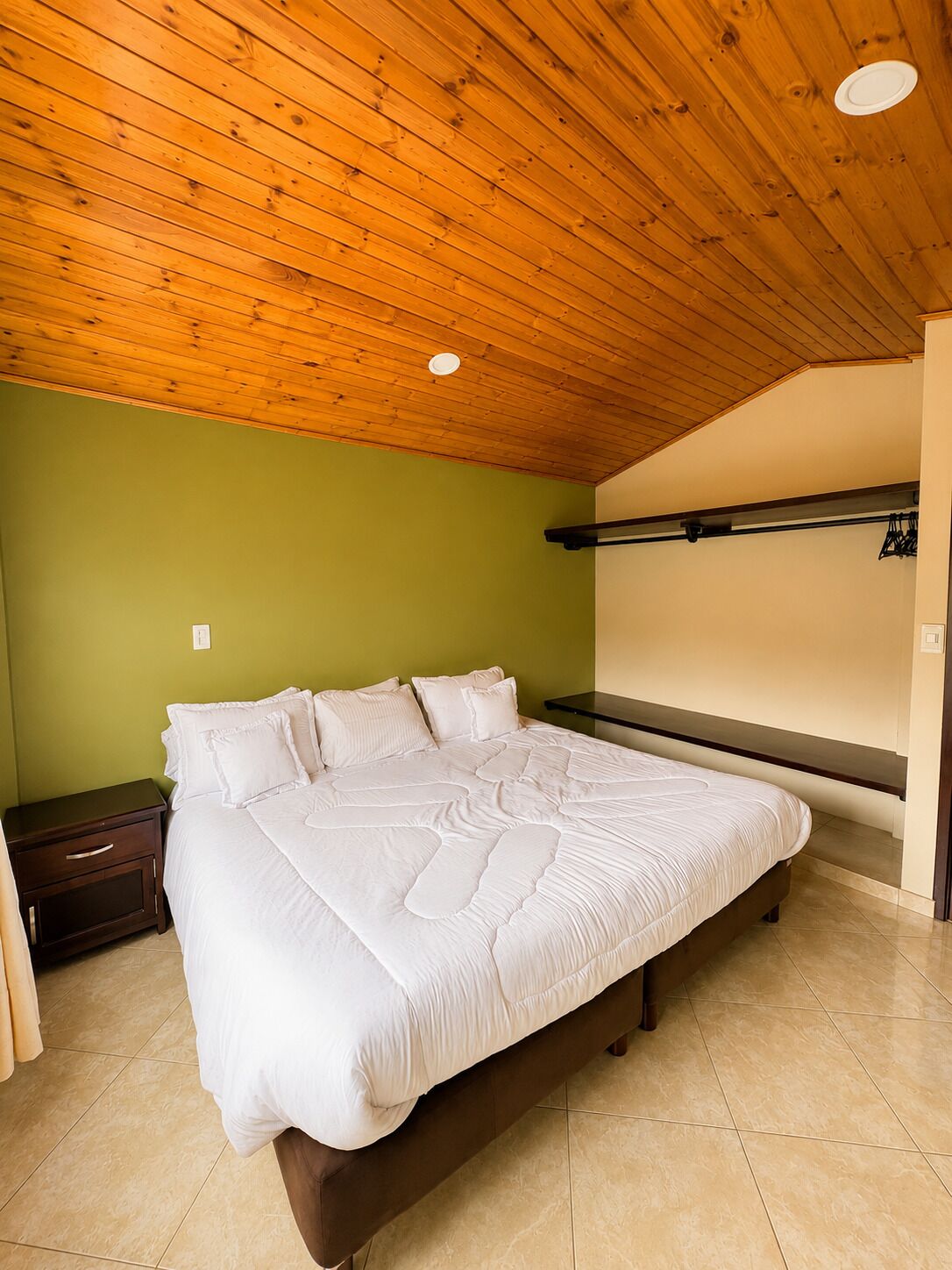Um quarto com uma cama grande, teto de madeira e parede verde.