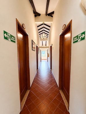 Un pasillo con puertas de madera, letreros de salida de emergencia verdes y un candelabro.