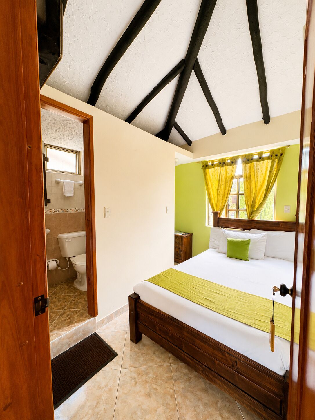 Un dormitorio con cama de madera, pared verde y ventana con cortinas amarillas.