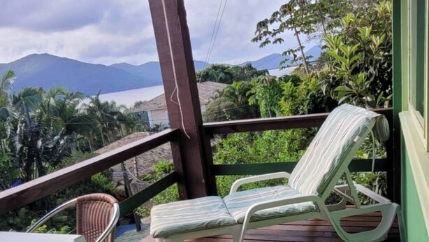 Une terrasse en bois avec une table et deux chaises en osier, offrant une vue sur un paysage montagneux.
