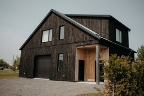 Un edificio moderno de dos pisos con un gran portón de garaje, fachada de madera y techo inclinado.