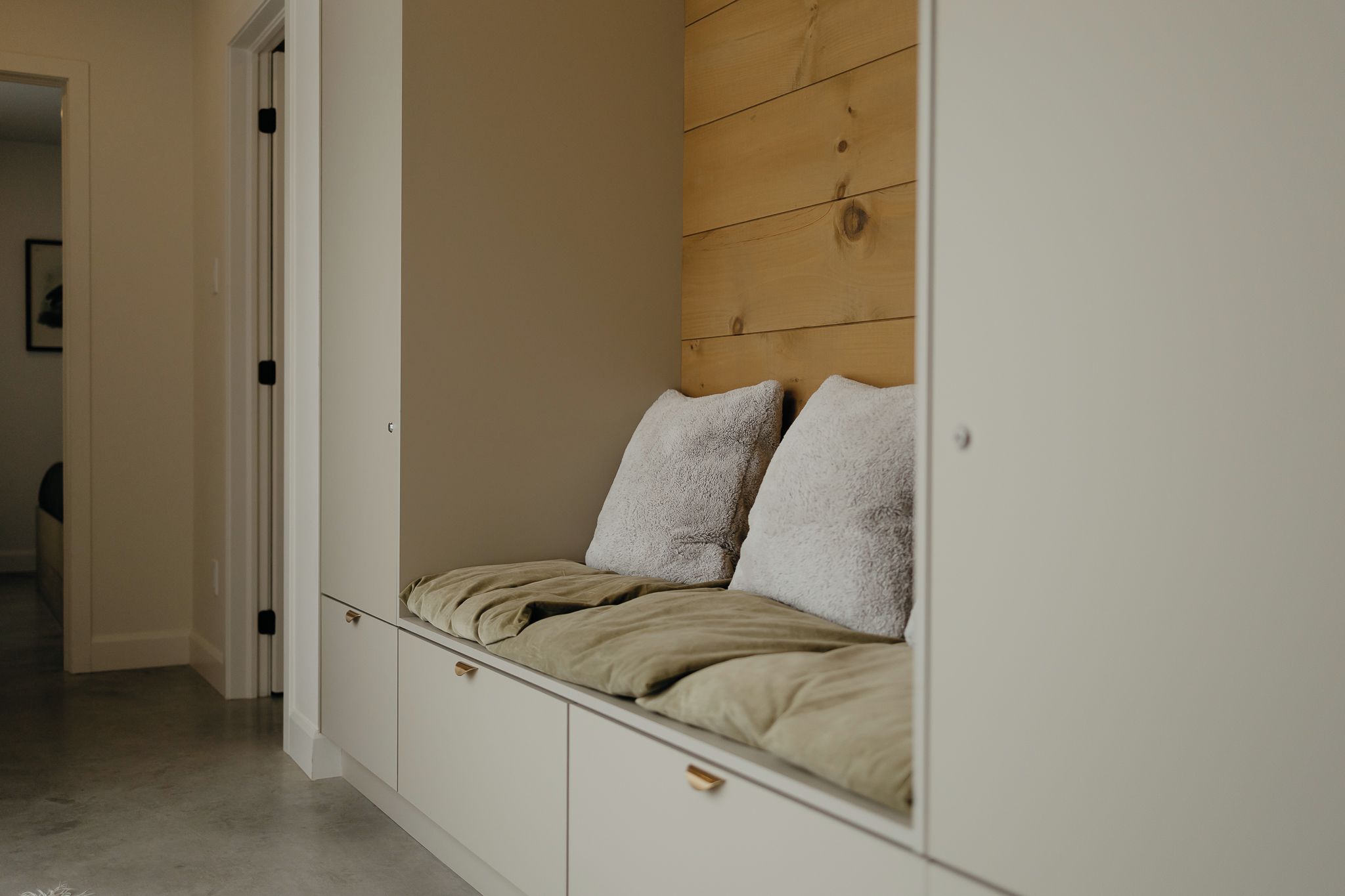 Un dormitorio con un banco empotrado, un revestimiento de pared de madera y un armario blanco.