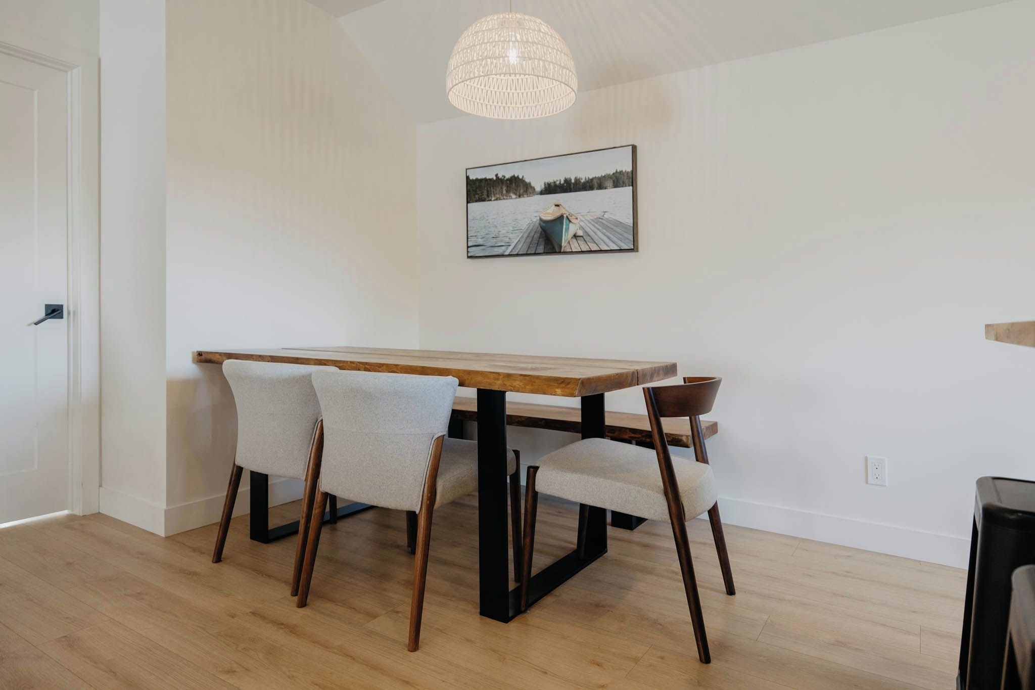 A dining area with a wooden table and four chairs, a pendant light, and a framed picture on the wall.