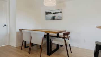 A dining area with a wooden table and four chairs, a pendant light, and a framed picture on the wall.