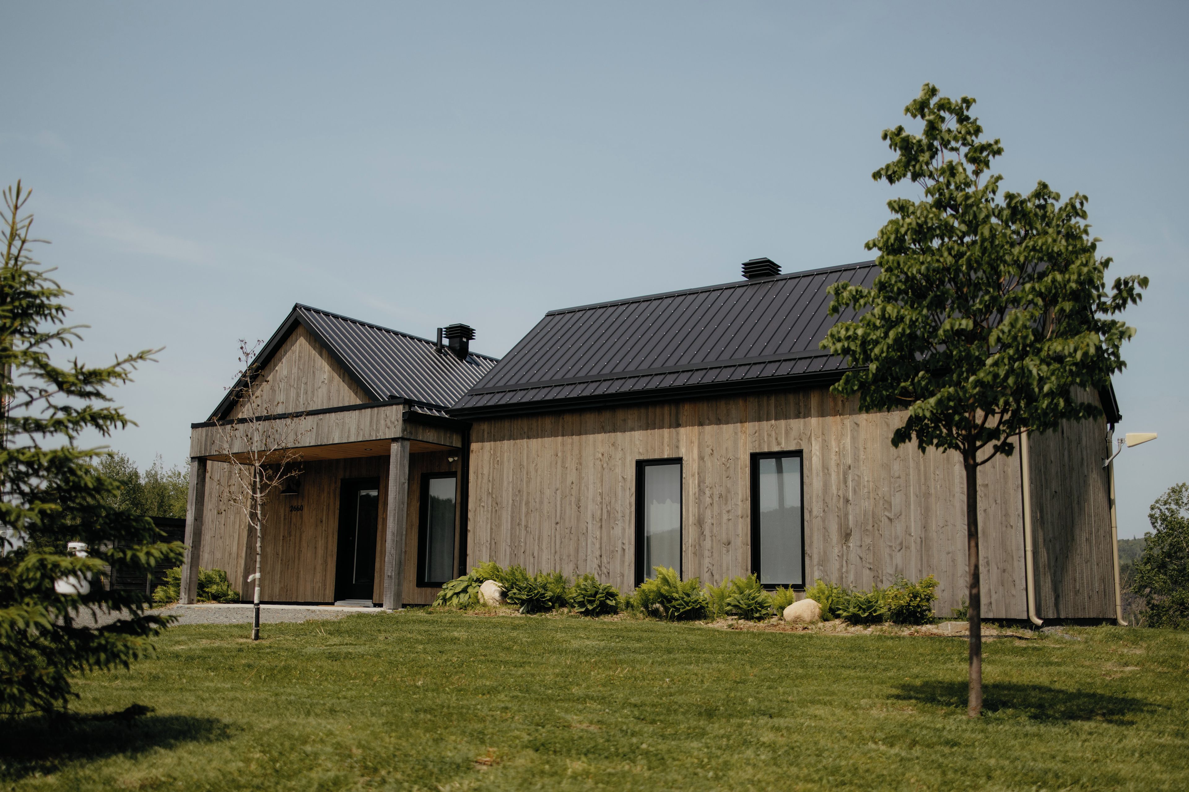 A modern wooden house with a sloped roof, large windows, and a well-maintained lawn.