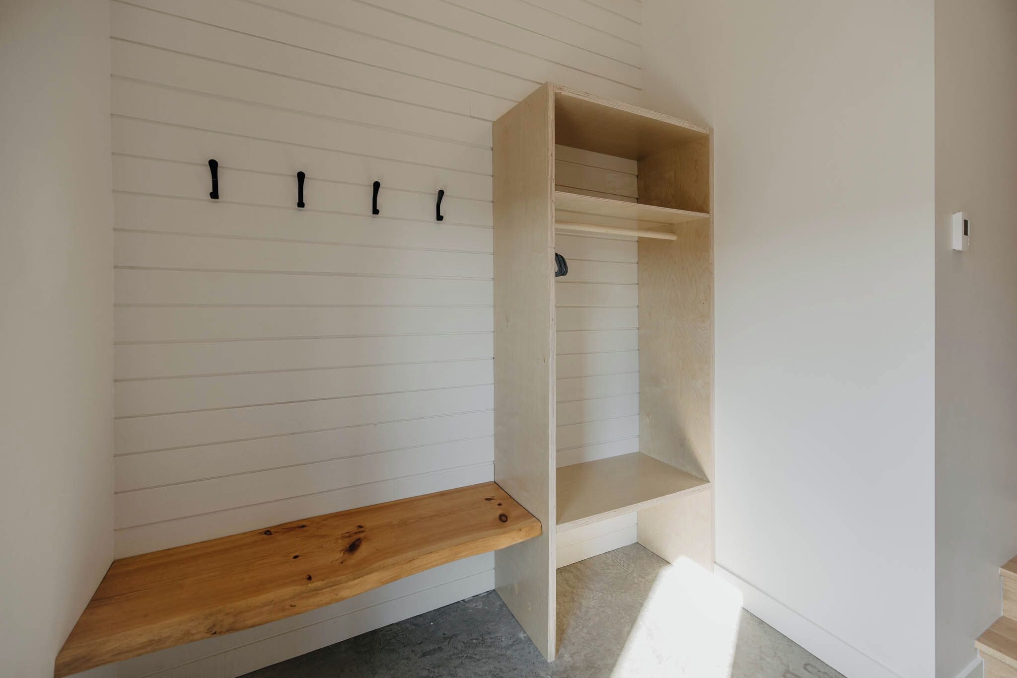 A room with a wooden bench, a built-in bench, and a wall-mounted coat rack.