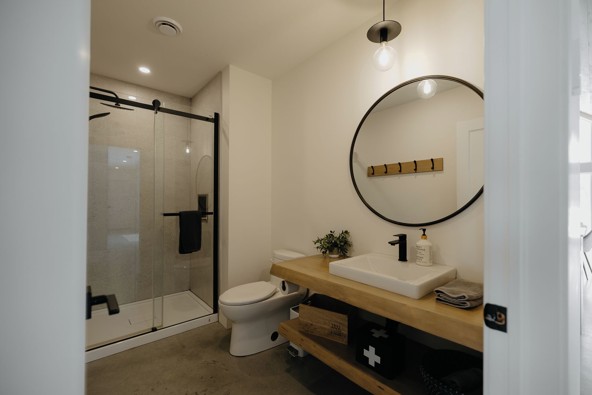 A modern bathroom with a glass shower enclosure, a white toilet, a wooden vanity with a sink, and a mirror with a wooden frame.