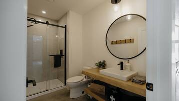 A modern bathroom with a glass shower enclosure, a white toilet, a wooden vanity with a sink, and a mirror with a wooden frame.