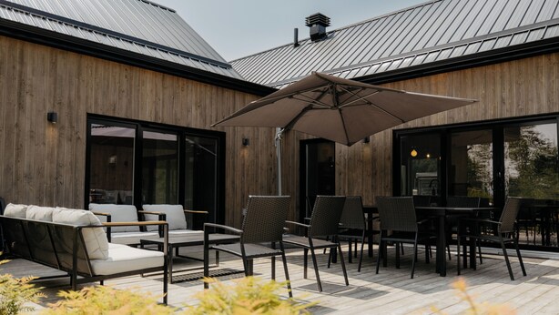 En træterrasse med udendørs møbler, heriblandt en sofa og stole, samt en stor parasol.