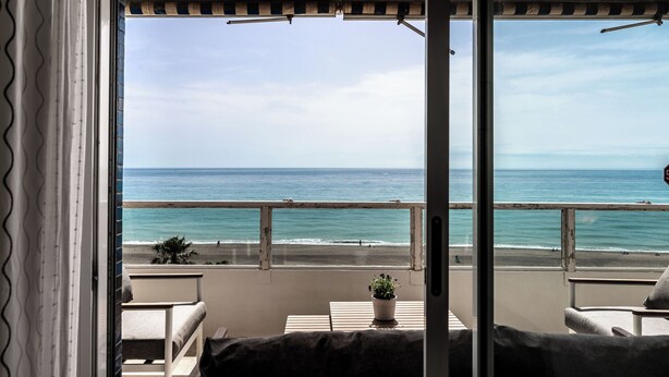 Ein Balkon mit Blick auf den Strand, einer Topfpflanze und einem Tisch.
