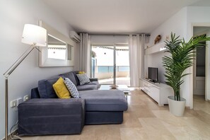 Un salon moderne avec un canapé, une lampe sur pied, un téléviseur et une plante en pot.