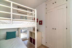 Un lit superposé avec un lit inférieur, une armoire blanche et un petit meuble de rangement.