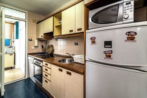 A kitchen with a microwave, refrigerator, sink, and wooden cabinets. - LXR La Carihuela Sea Views 3-Bedroom (Torremolinos)