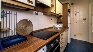 Eine Küche mit Holzschränken, einem schwarzen Induktionskochfeld, einer Edelstahl-Spüle und einem Kühlschrank.
