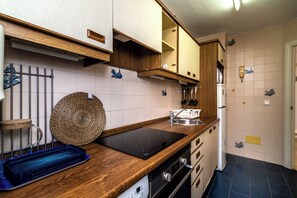 Eine Küche mit Holzschränken, einem schwarzen Induktionskochfeld, einer Edelstahl-Spüle und einem Kühlschrank.