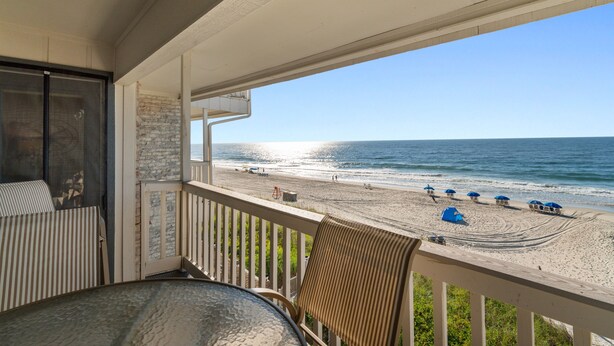 Ein Balkon mit Blick auf den Strand, inklusive Tisch und Stühlen.