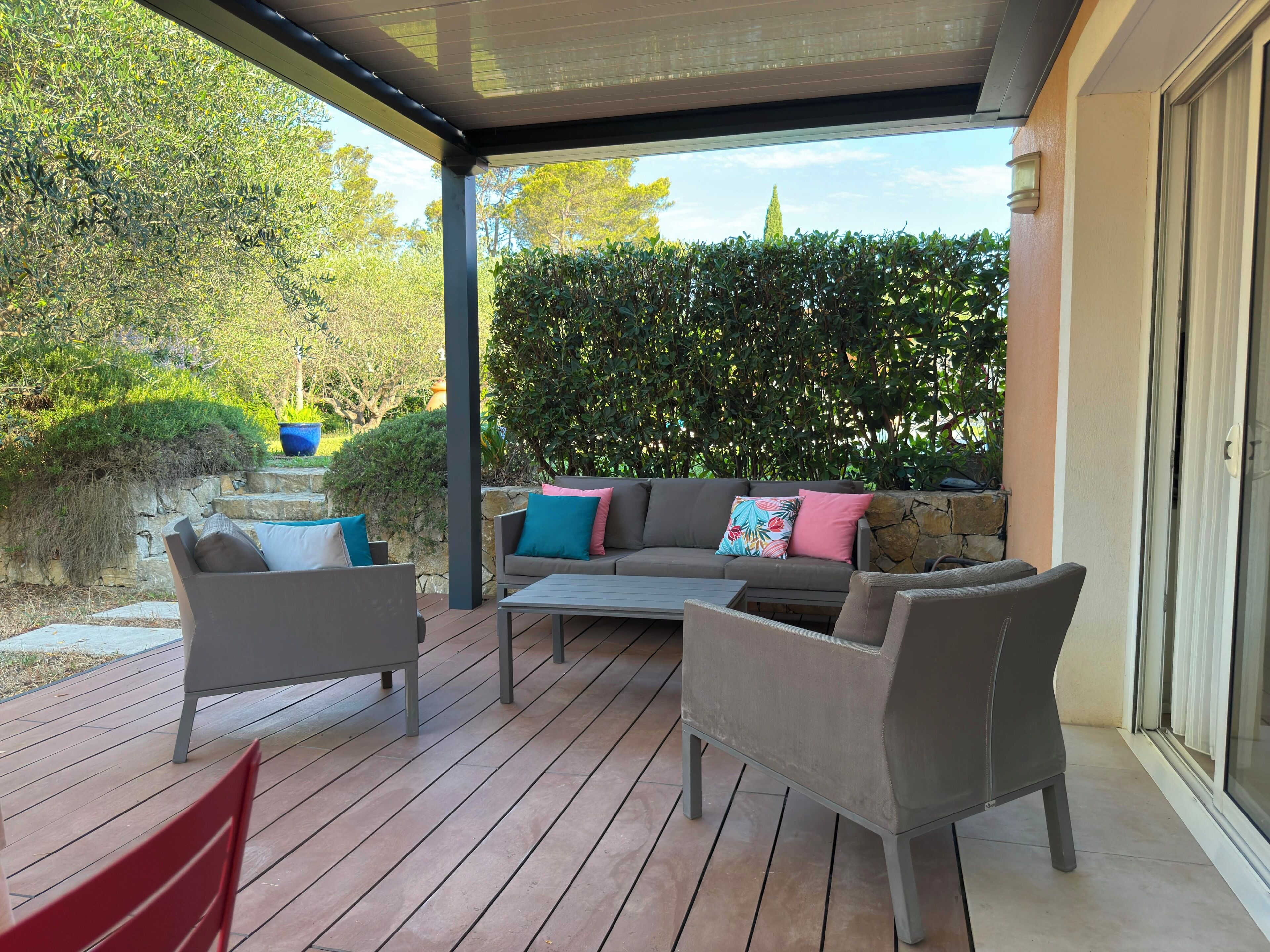 Une terrasse extérieure dotée d’un espace salon couvert, d’un escalier en pierre et offrant une vue sur le jardin environnant.