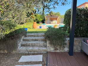 Un escalier en pierre menant à une terrasse en bois, une piscine et un bâtiment doté d’un toit en tuiles.