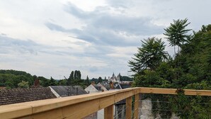 Holzgeländer eines Balkons mit Blick auf ein Wohngebiet, mit Häusern und einem schlossähnlichen Gebäude in der Ferne.
