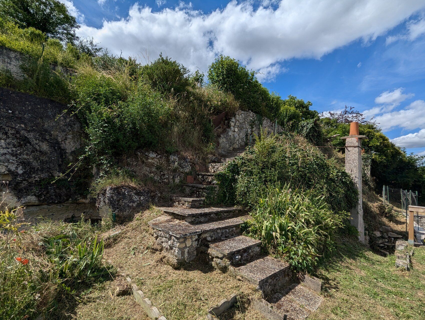 Ancient stone steps leading up a hill, surrounded by greenery and a stone wall.