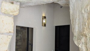 Ein Raum mit Steinwänden, zwei schwarzen Türen, einer strukturierten Decke und einer kleinen Wandleuchte.