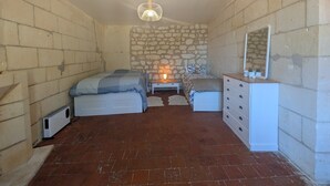 Ein Schlafzimmer mit Backsteinboden, einem Bett mit blauer Decke, einem Nachttisch mit Lampe, einem Schminktisch und einer Steinwand.