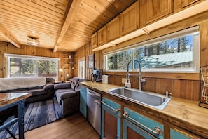 A wooden cabin interior with a kitchen, dining area, and large windows. - Sawmill Trail Tahoe Cabin (South Lake Tahoe)