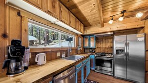 Eine Holzhütte mit einer Küche, inklusive Kaffeemaschine, Spüle, Herd und Kühlschrank.
