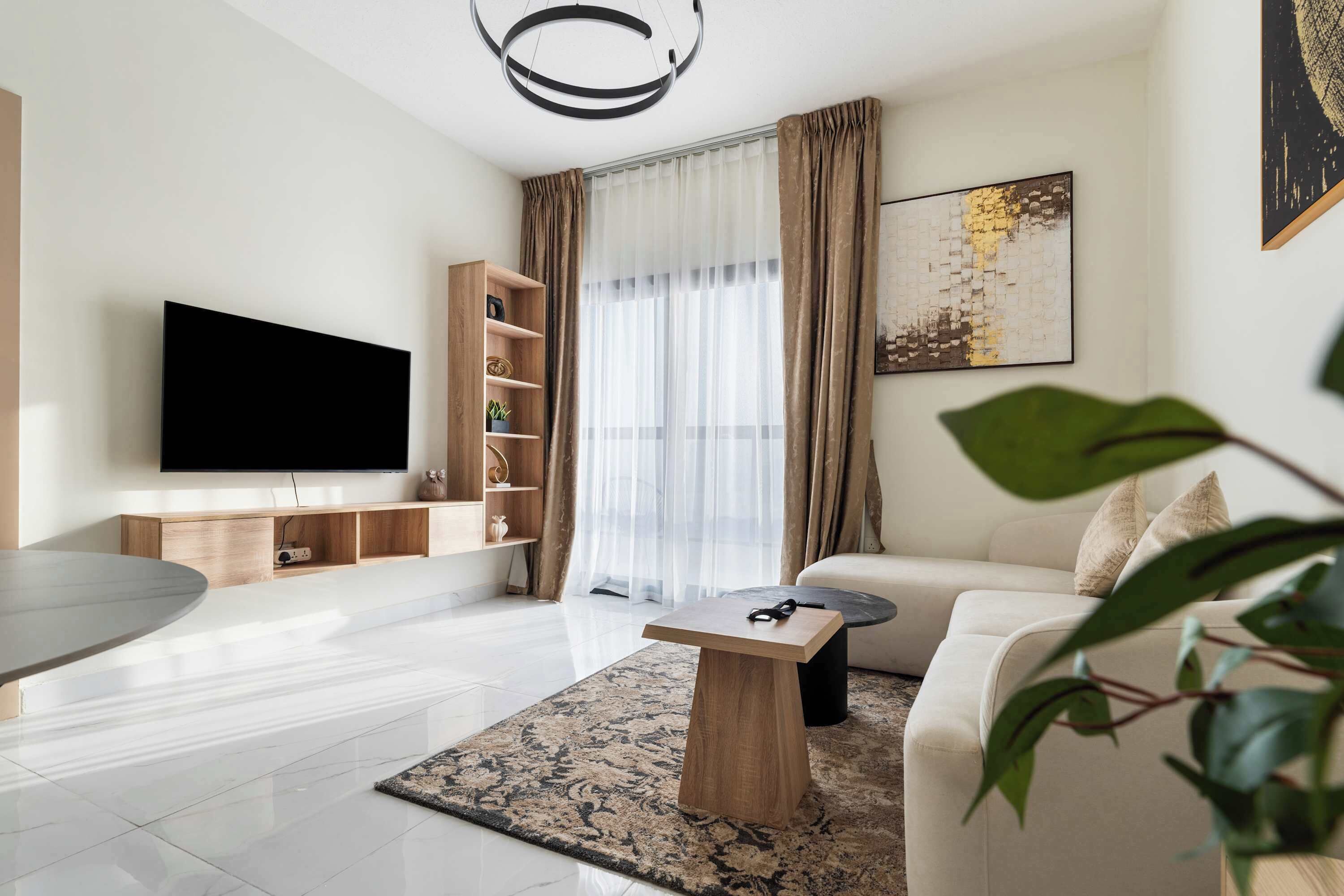 A modern living room with a flat-screen TV, a wooden coffee table, a sofa, a bookshelf, and a large window with curtains.