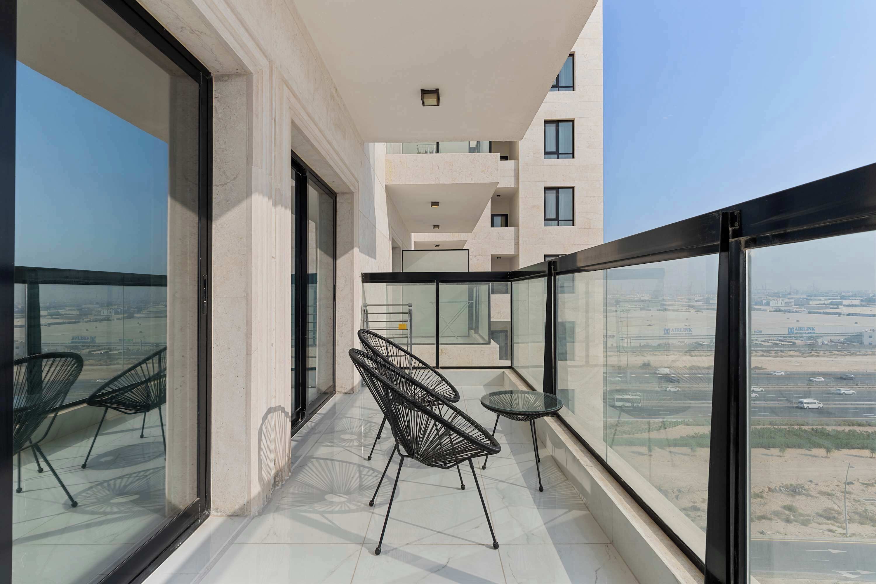 A balcony with two chairs and a small table, a view of a cityscape, and a building with multiple floors and balconies.
