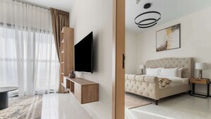 Une chambre d’hôtel moderne avec un grand lit, un téléviseur à écran plat fixé au mur, une console en bois et une grande fenêtre agrémentée de rideaux légers.