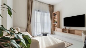 Un salon moderne avec un canapé, un téléviseur, une étagère en bois et une grande fenêtre avec des rideaux.