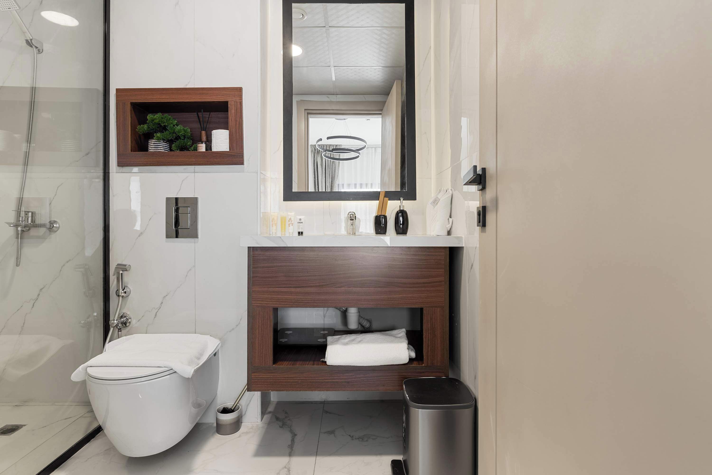 A modern bathroom with a glass shower enclosure, a toilet, a vanity with a mirror, and a trash bin.