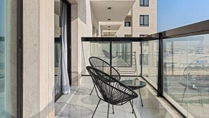 Un balcon avec deux chaises noires, une table en verre et une vue sur un immeuble à étages multiples.