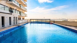 Une piscine sur le toit offrant une vue dégagée sur les gratte-ciel de la ville, un bâtiment moderne doté de balcons et une enseigne indiquant « APPAREL GROUP ».
