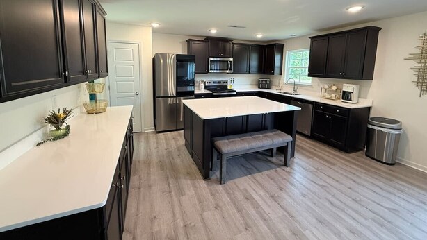 A modern kitchen with dark cabinets, a central island, and built-in appliances. - 5 bedroom spacious in quiet neighborhood (Greensboro)