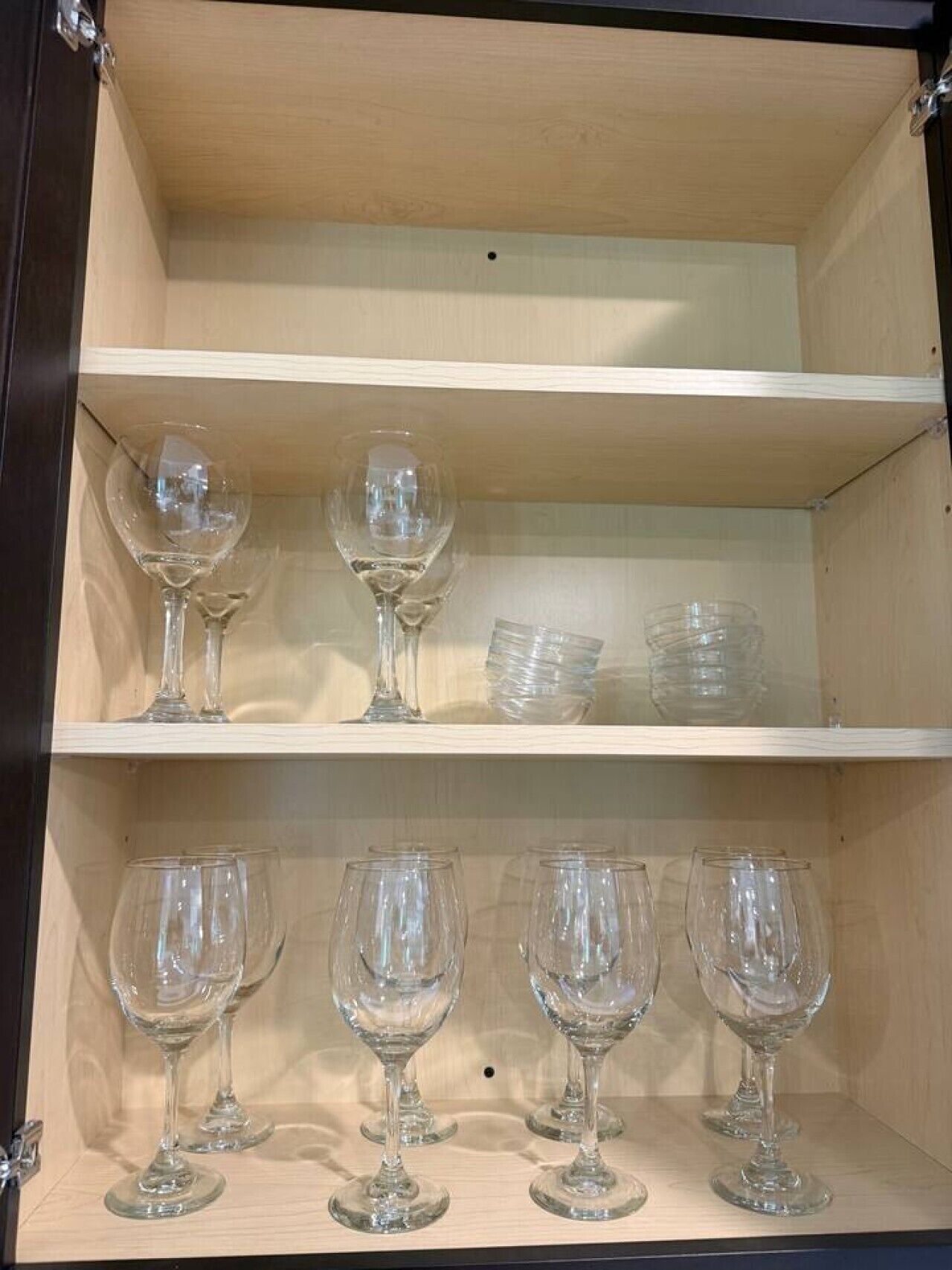 A wooden cabinet with shelves containing wine glasses and clear glass bowls.