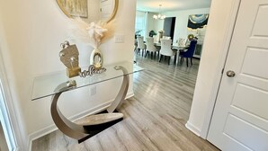 A hallway with a glass console table, a round mirror, and a 'Welcome' sign. - 5 bedroom spacious in quiet neighborhood (Greensboro)