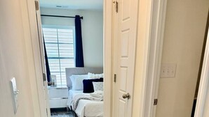 A hallway leading to a bedroom with a bed, a nightstand, and a window with blinds. - 5 bedroom spacious in quiet neighborhood (Greensboro)