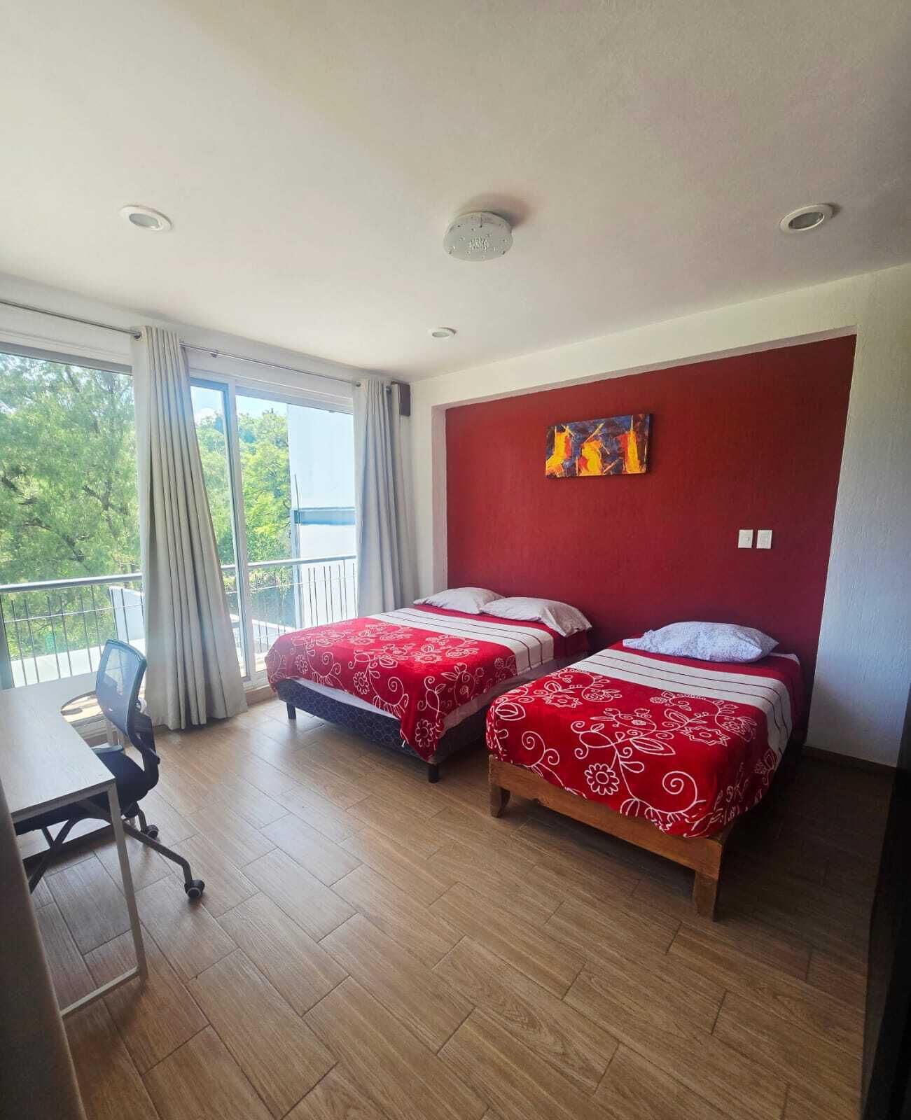 A hotel room with two beds, a desk, and a balcony with a view.