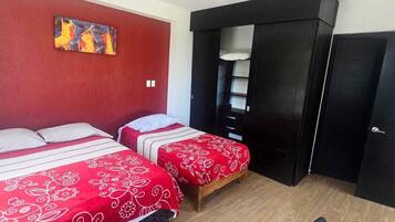 A room with two beds, a desk, a chair, a wardrobe, and a painting on the wall.