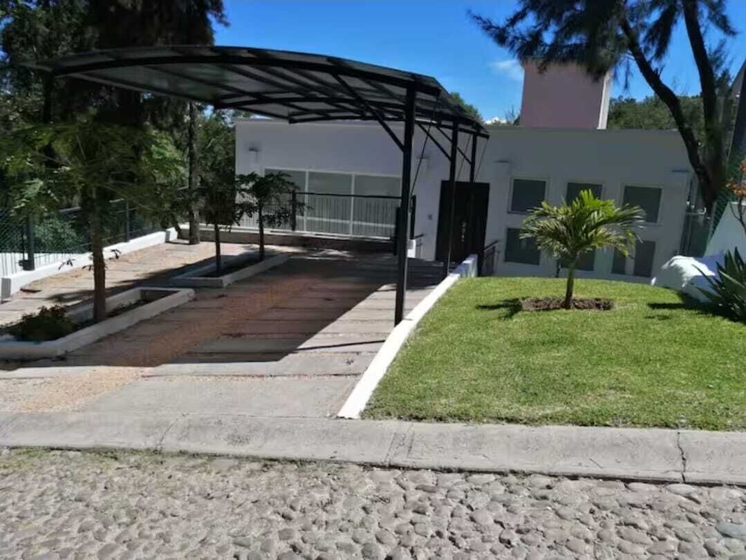 A covered outdoor area with a paved walkway, a small lawn, and a building in the background.