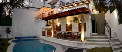A modern house with a swimming pool, a covered patio, and a staircase leading to the upper level.