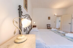 Um quarto com uma cama, uma mesa de cabeceira com abajur, uma cadeira e uma porta.