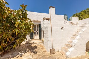Um edifício branco com porta, degraus e um jardim.