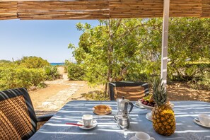 Mesa ao ar livre com vista para o mar, rodeada por vegetação e uma pérgula de bambu.