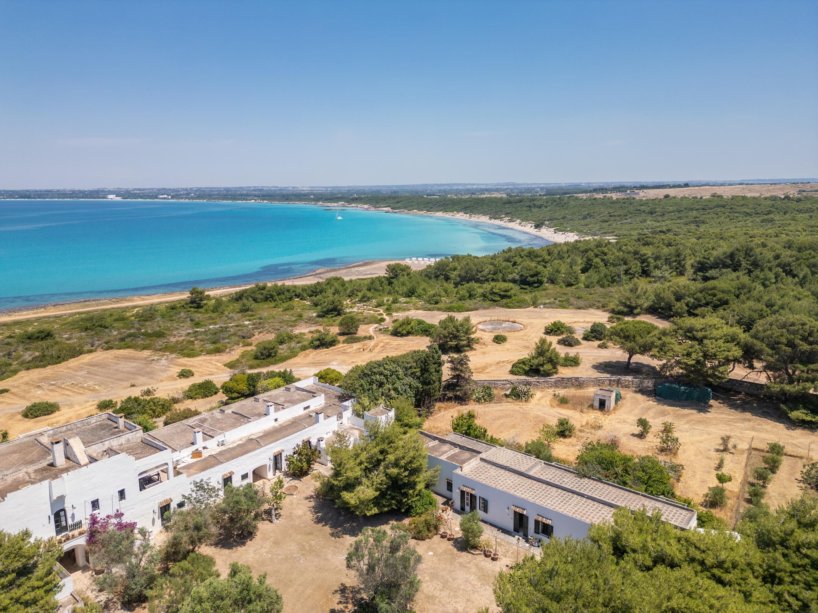 A coastal property with a white building, a beach, and surrounding greenery.